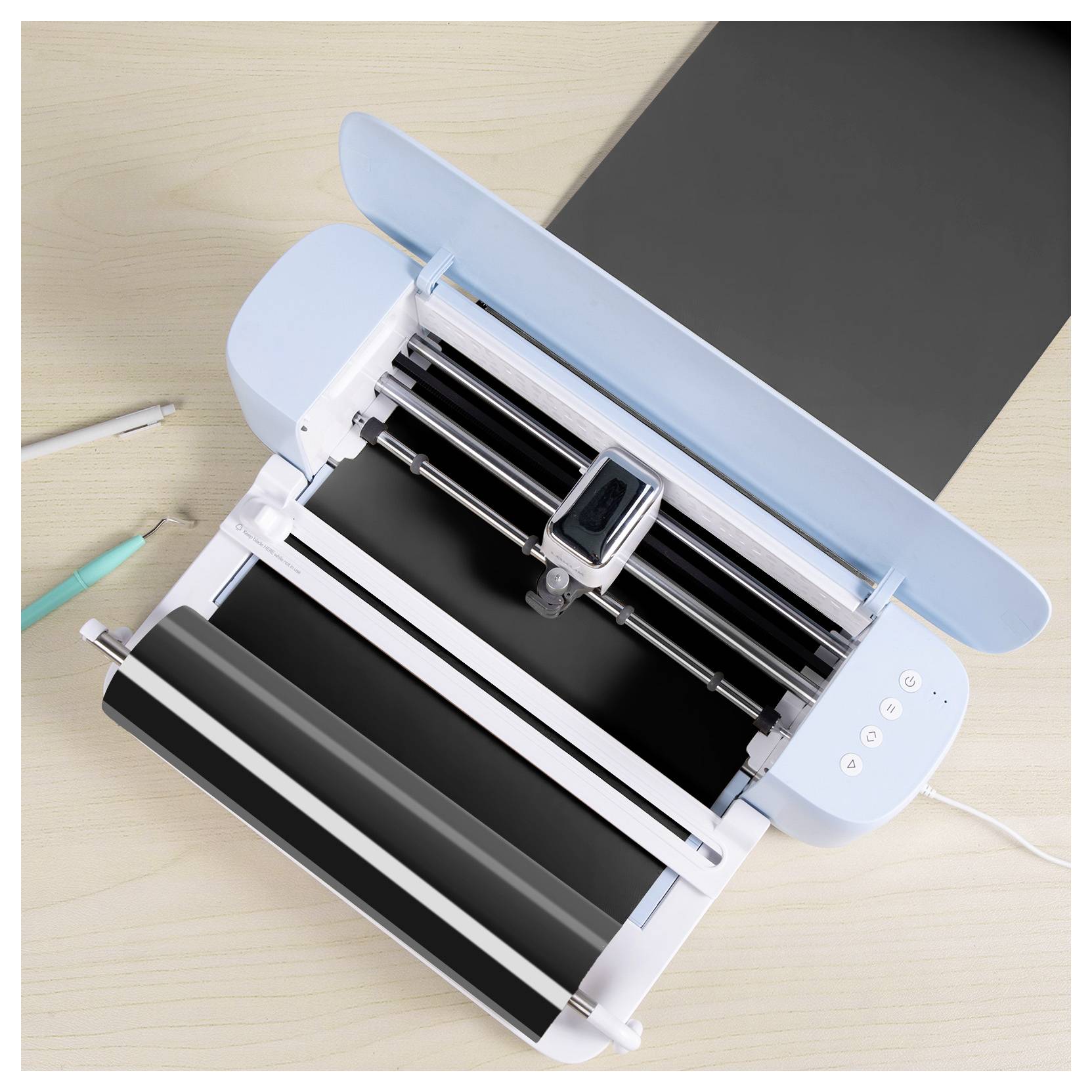 A cutting machine on a wooden table, open and ready to operate, with two pens nearby.