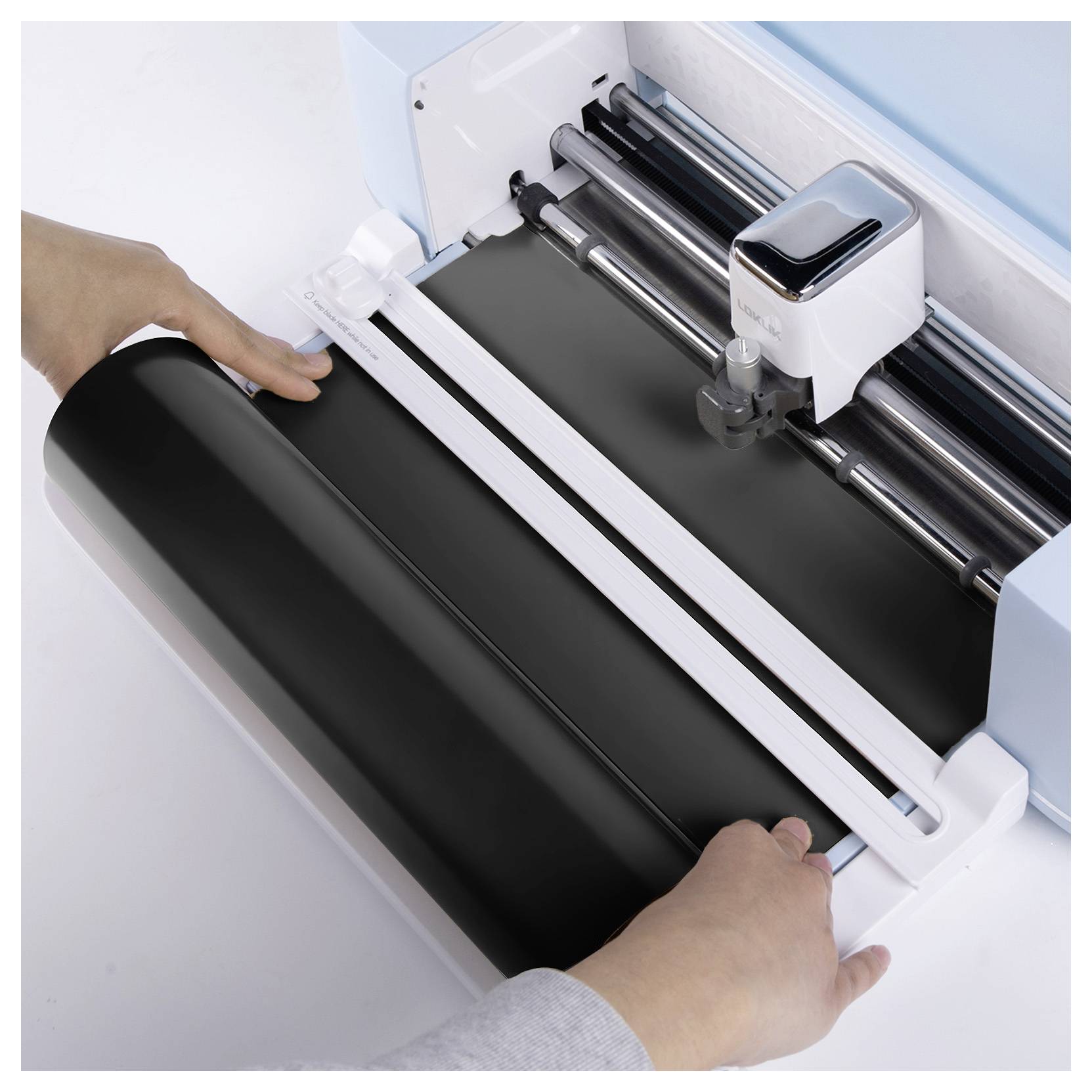 Hands preparing a black roll of material on a cutting machine, which is ready for operation, suggesting a crafting or design project.