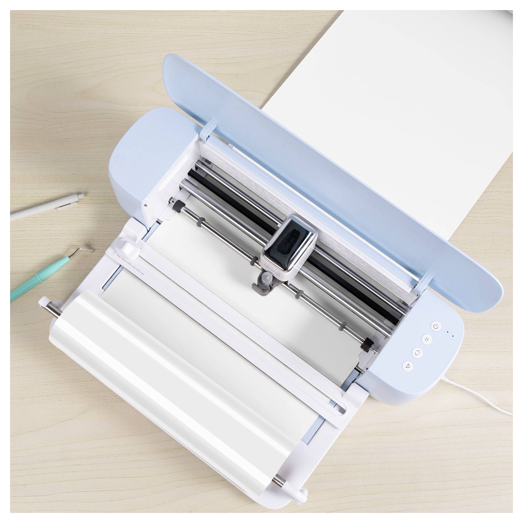 A digital cutting machine on a desk with a light blue lid and a roll of white material loaded, ready for crafting or design projects.