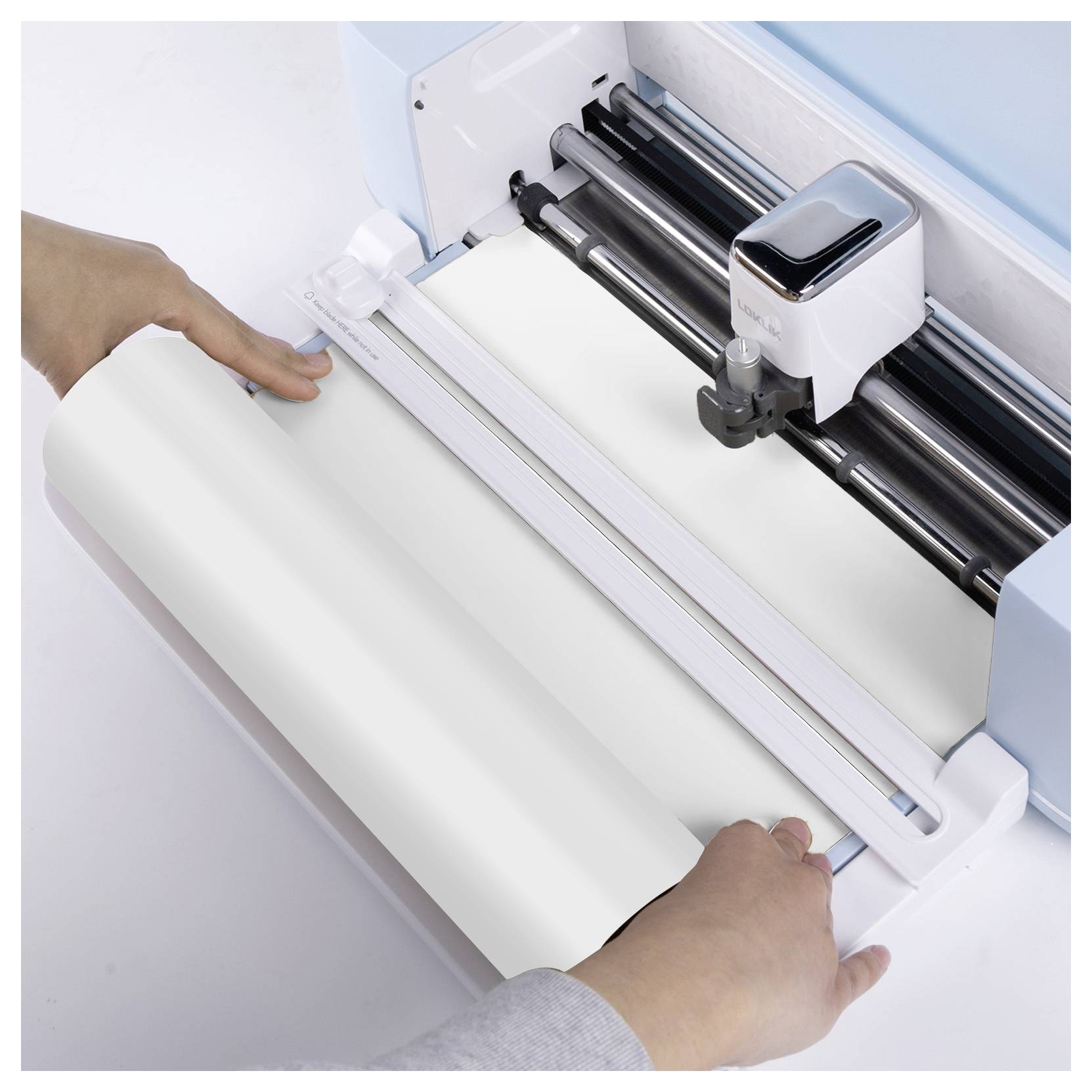 A person is loading a roll of material into a cutting machine, preparing it for a crafting or design project.