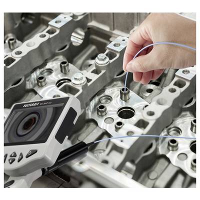 Hand holding a blue probe into a metal engine component while a borescope camera inspects the inside of the part.<br>