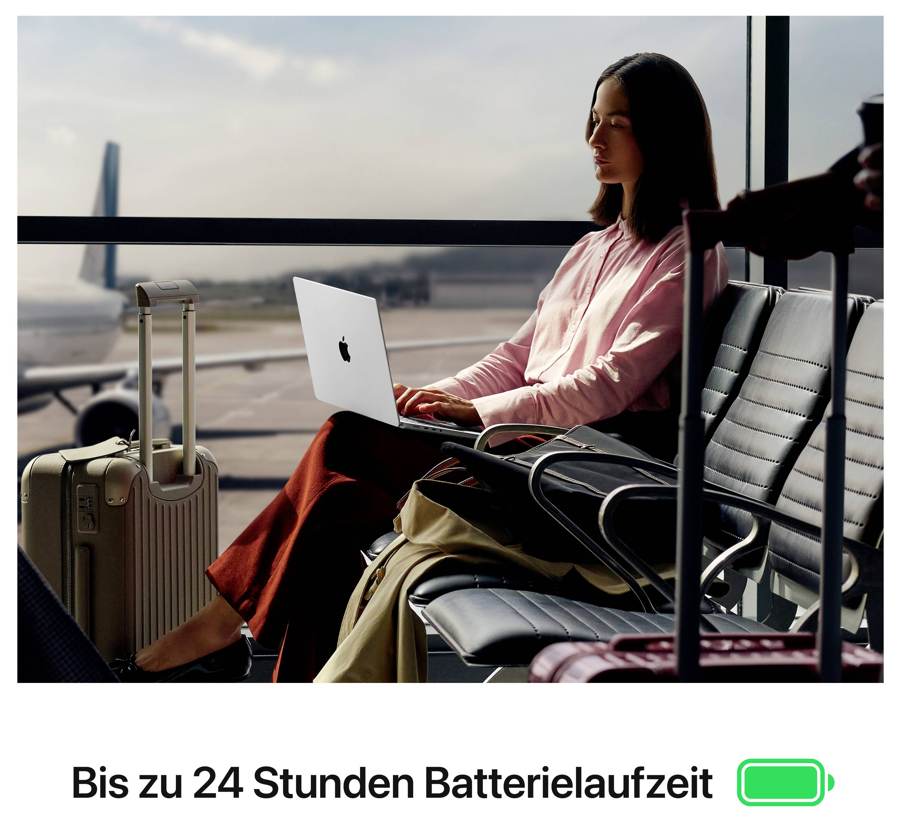 Woman working on laptop at airport, next to suitcase and luggage; at the bottom it says 'Up to 24 hours battery life' next to battery symbol.