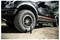 Black off-road pickup truck with a flat front tire; a small air compressor is attached by a hose for inflating the tire.<br>