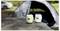 Two Konau Air water bottles on a tree stump in front of a camping tent outdoors.<br>