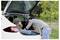 Two people load a blue bag into the open trunk of a white car outdoors.