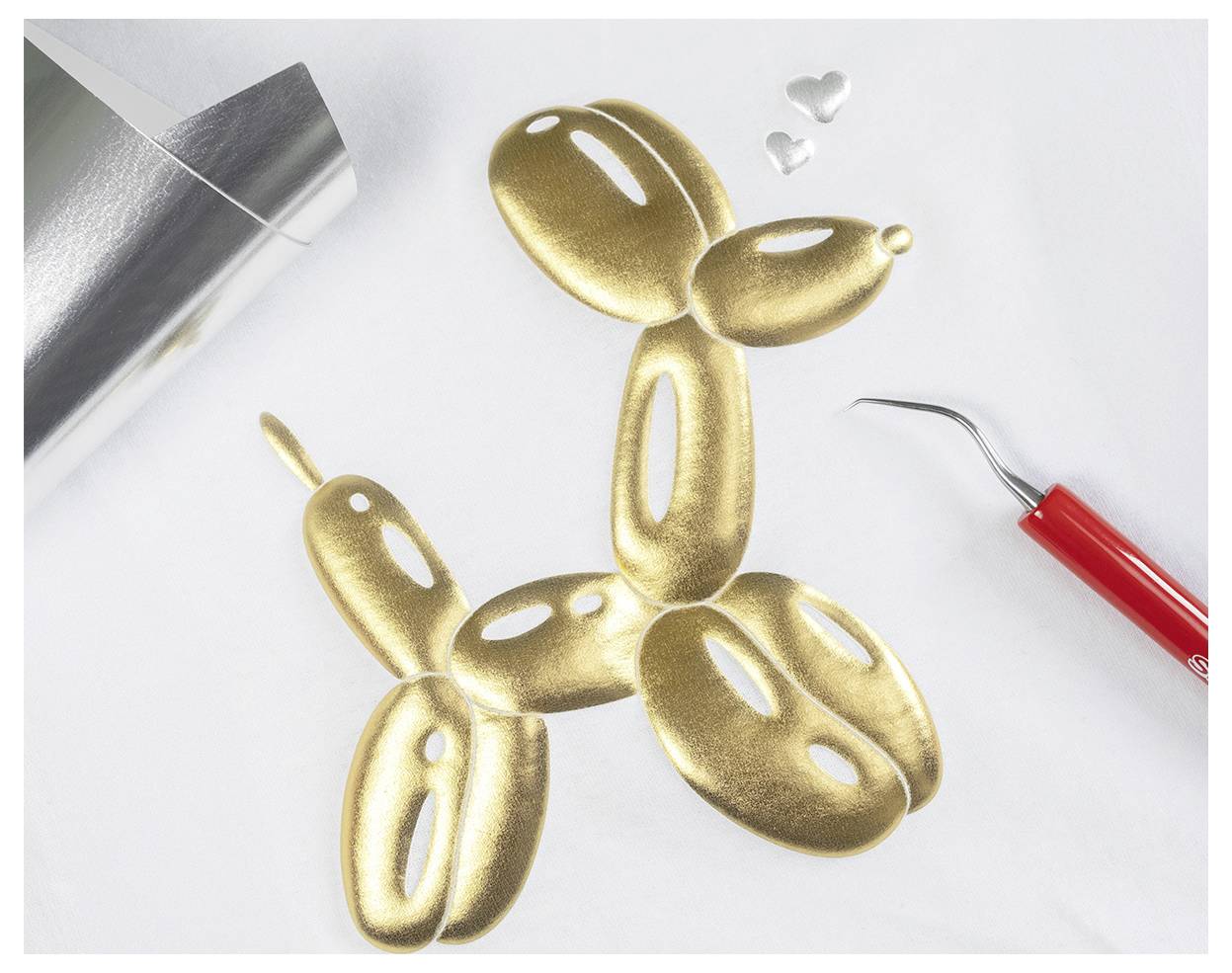 A gold balloon animal dog on a white surface with foil and a red tool nearby.