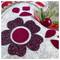 A close-up of a decorative holiday ornament featuring a glittery flower design on felt, with red accents and faux greenery.