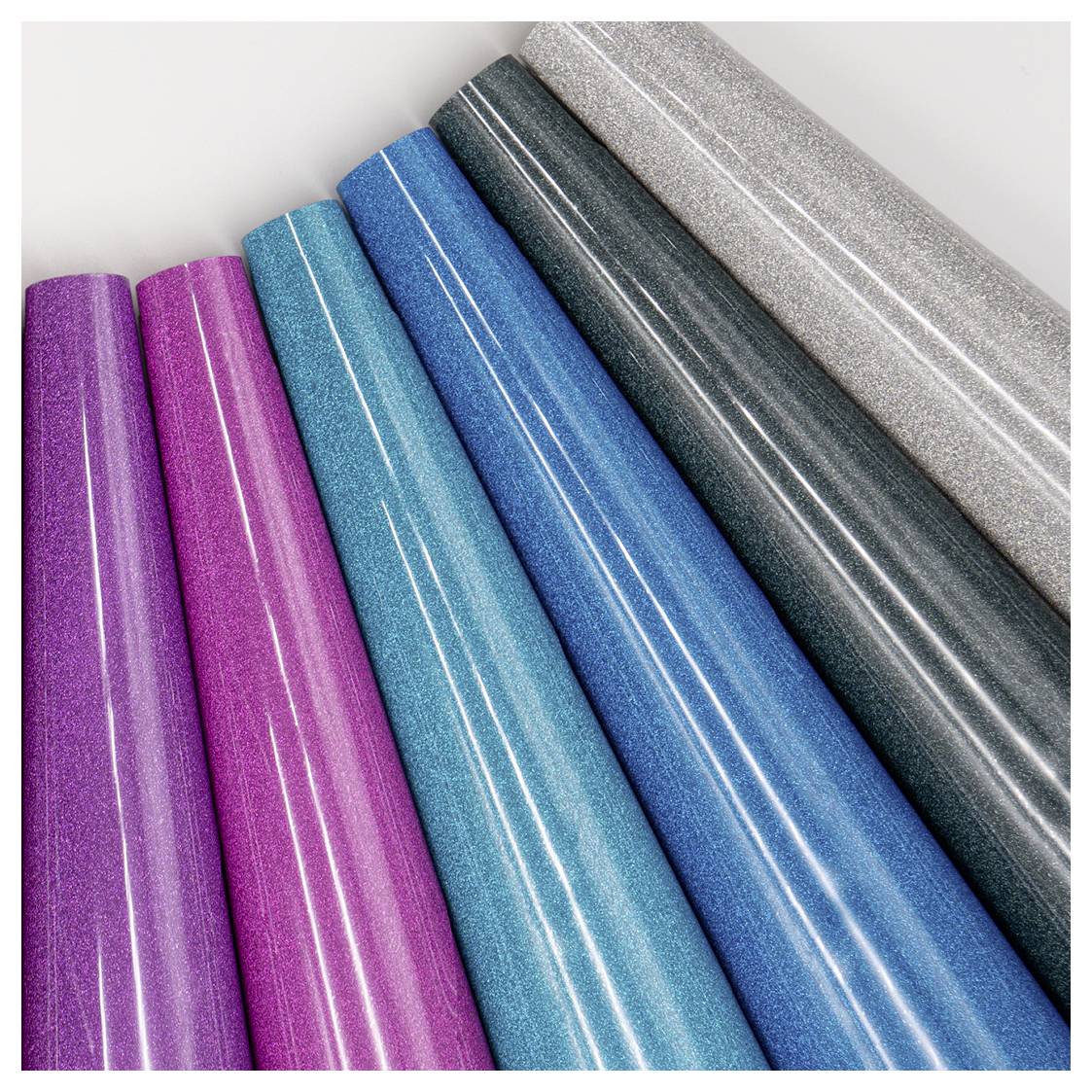 Six rolls of colorful, shiny wrapping paper arranged diagonally; colors include purple, pink, blue, turquoise, gray, and silver.