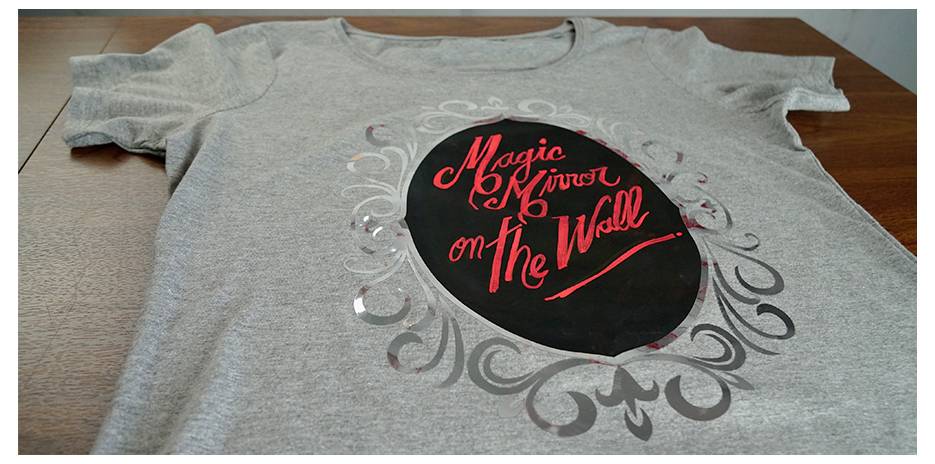 A gray T-shirt with an ornate black oval design featuring the red text 'Magic Mirror on the Wall'.
