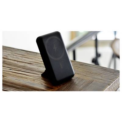 A black wireless charger with a stand, showing a charging symbol, placed on a wooden table.