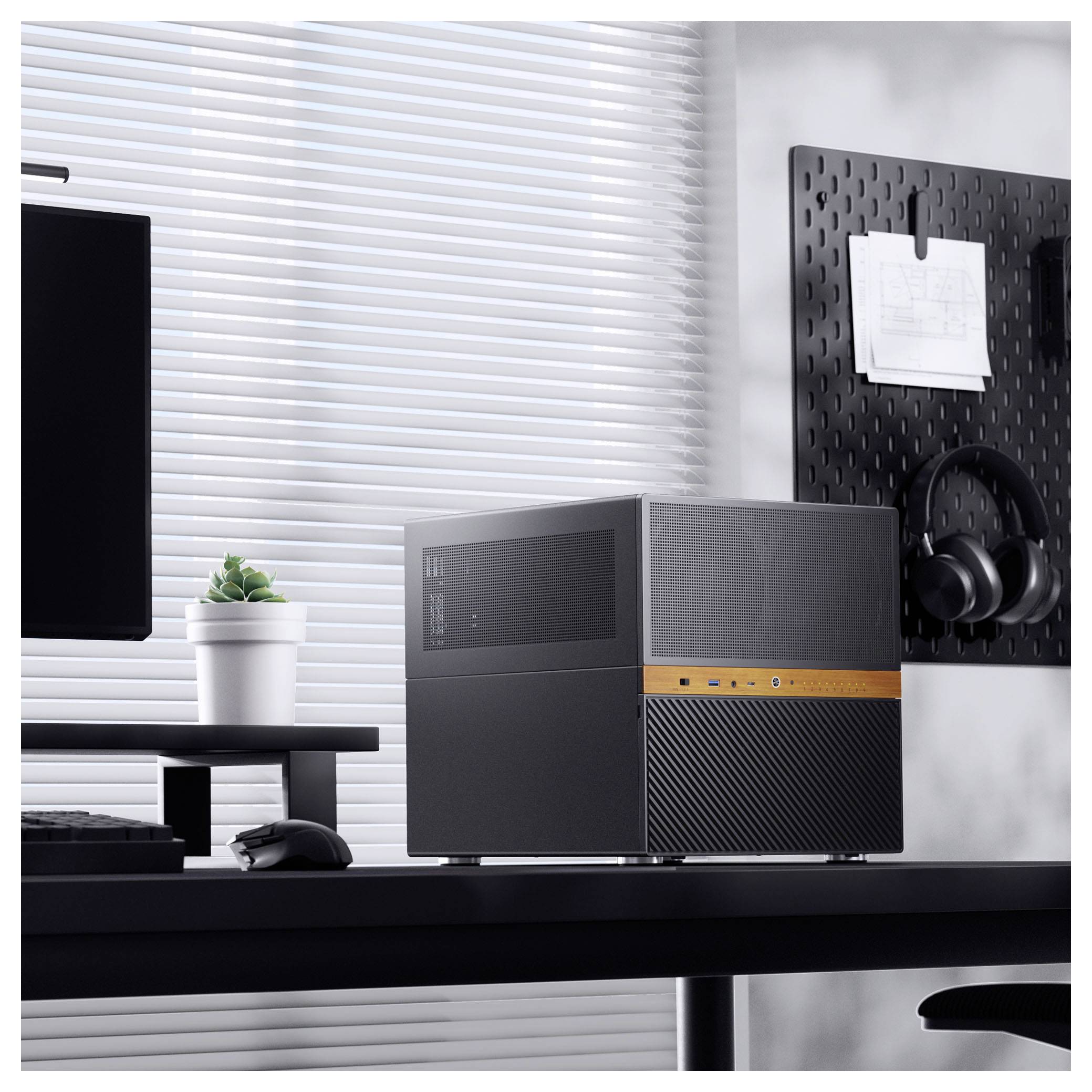 A modern desktop computer on a table, with a plant and a headphone on a wall pegboard, in a well-lit room with blinds.