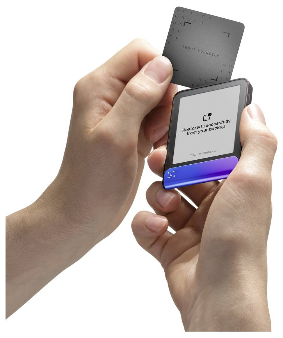 Person holding a small device and a card, with the device screen reading 'Restored successfully from your Backup'.