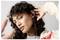 A person with curly hair is wearing wireless earbuds, posing playfully with their hands near their head, looking directly at the camera.