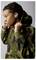 A person wearing a camouflage hoodie and wireless earbuds, adjusting the hood while turned to the side, against a plain background.