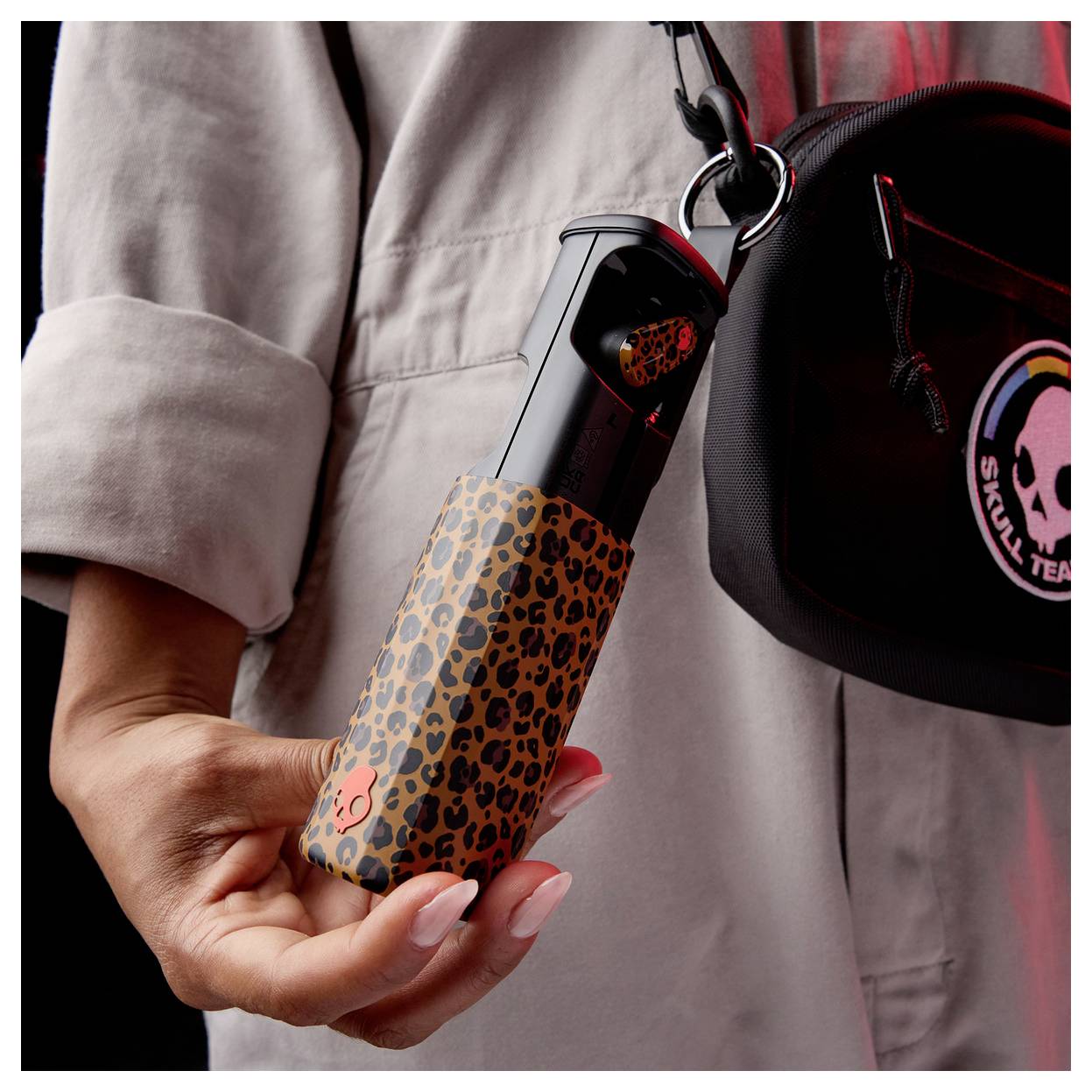 A person holding a compact umbrella with a leopard print cover, attached to a black bag with a logo reading 'Skull Team'.