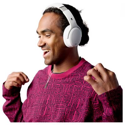 A person wearing a patterned red sweater and white headphones smiles, appearing to enjoy music.