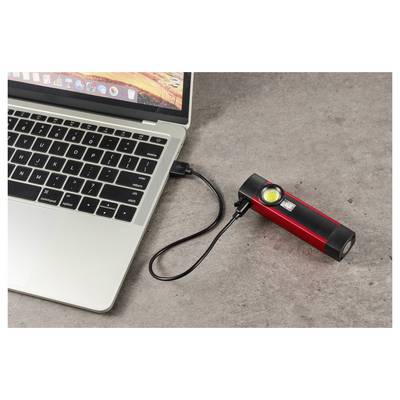Laptop connected by USB cable to a red portable power bank with a lit indicator light on a tabletop.