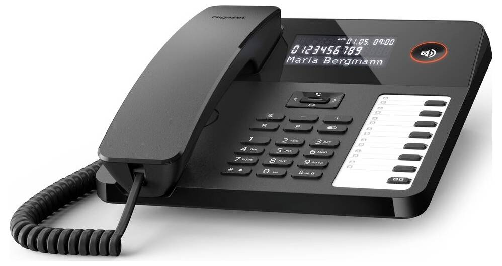 A black office desk phone with a digital display shows numbers '0123456789' and name 'Maria Bergmann', alongside numeric buttons and a coiled cord.