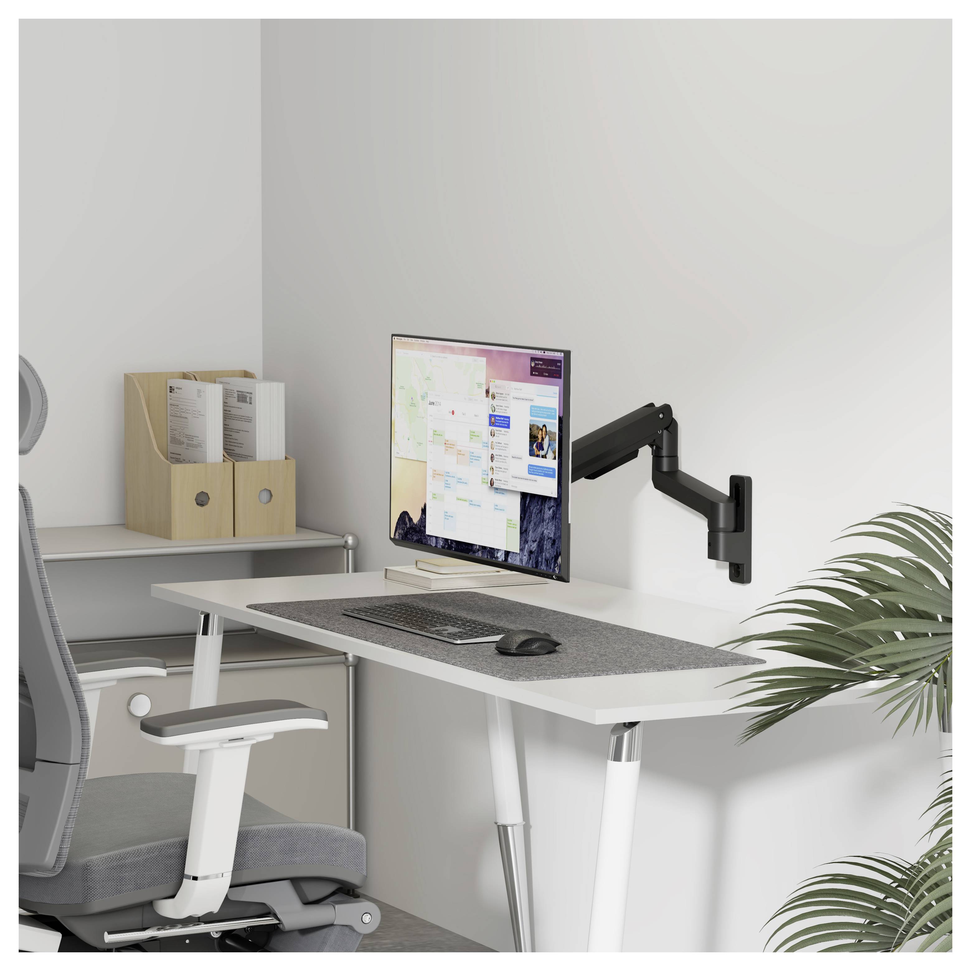 Modern home office with an adjustable desk, monitor on a wall mount, keyboard and mouse, chair, shelf with files, and a plant.