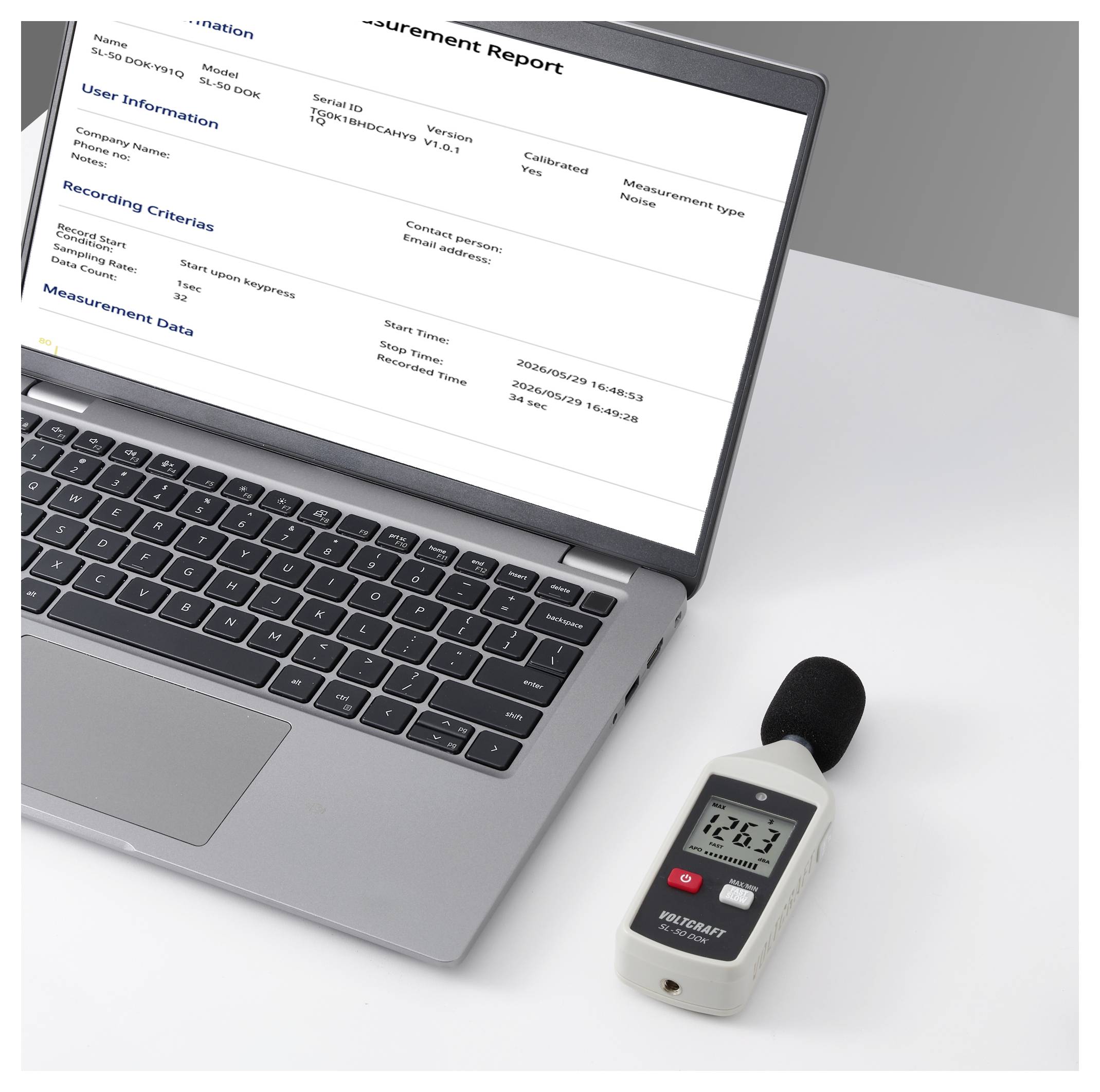 Laptop displaying a 'Measurement Report' beside a handheld sound level meter, indicating noise measurement data recording.