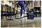 A person using a vacuum cleaner in a restaurant with wooden floors, empty tables, and chairs, suggesting cleaning before or after hours.