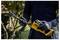 A person wearing gloves operates a DeWalt reciprocating saw outdoors, surrounded by greenery, demonstrating tool use.