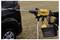 A person is using a yellow cordless pressure washer to clean a black vehicle in an outdoor setting.