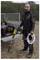 A person stands outdoors, wearing safety goggles and holding a pressure washer and hose, surrounded by tools and equipment on a trailer.