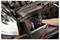 A person wearing a glove uses a tool to service an open car engine, highlighting a repair or maintenance activity.