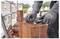 'A person wearing gloves cuts a blue strap on a stack of red roof tiles with a utility knife on a construction site.'