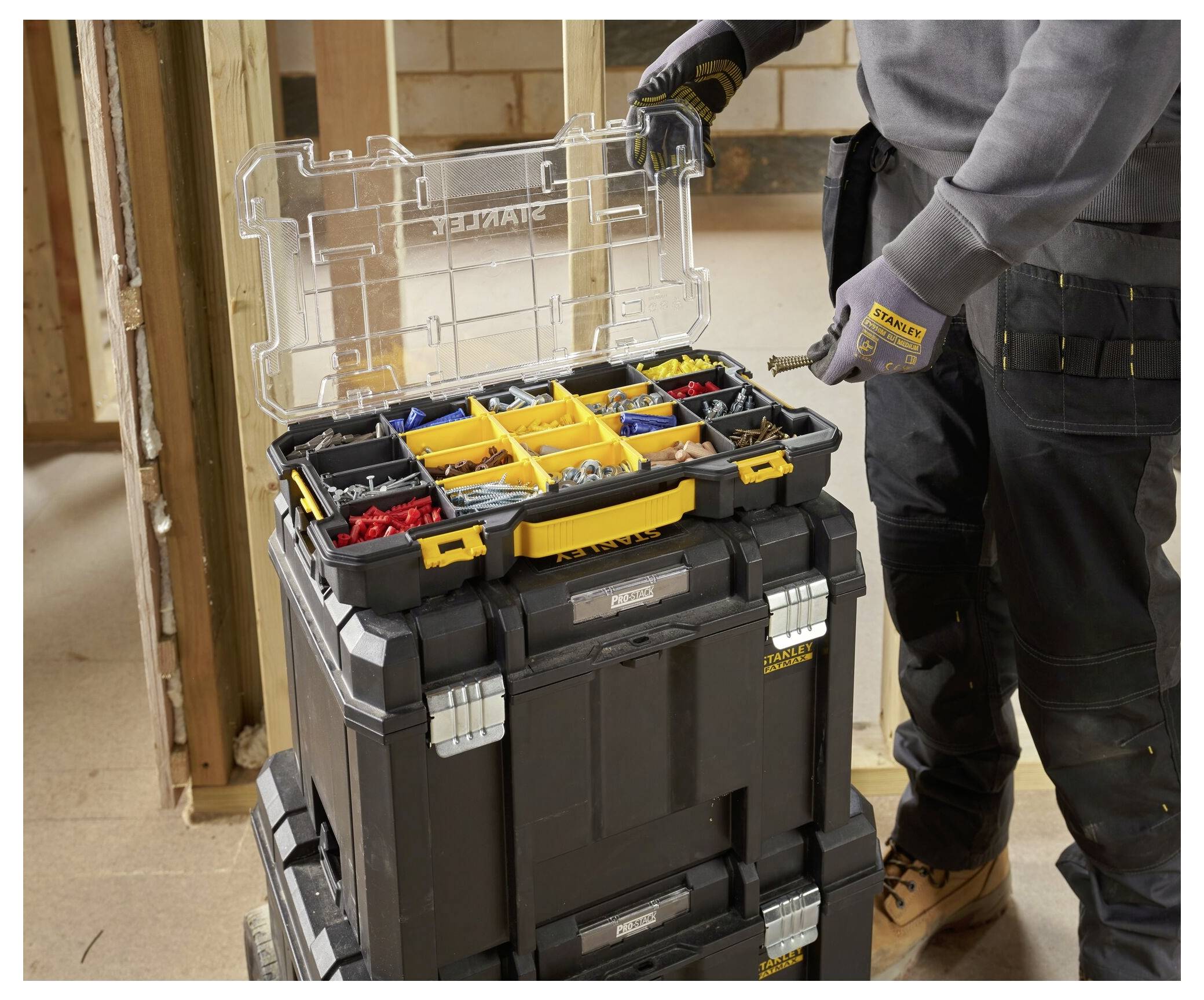 A person organizing various screws and bolts in a portable plastic storage box with multiple compartments, open lid showing contents.