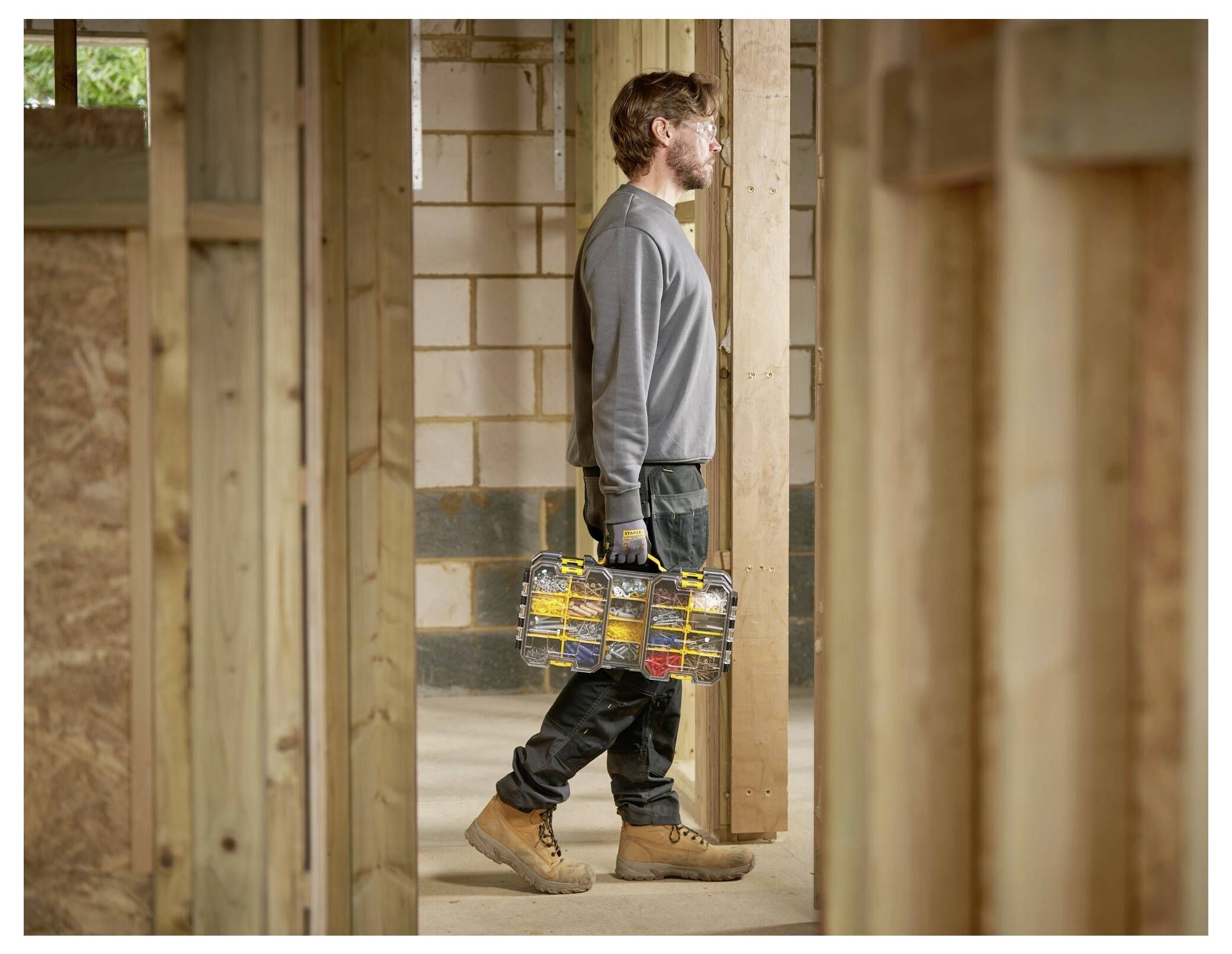 A person in work attire carrying a toolbox walks through a partially constructed building, suggesting construction or renovation work.