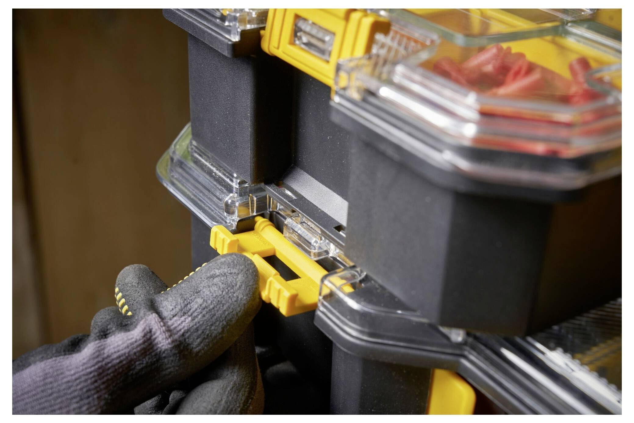 'A gloved hand clips together two black and yellow storage boxes, with red items visible in a compartment.'