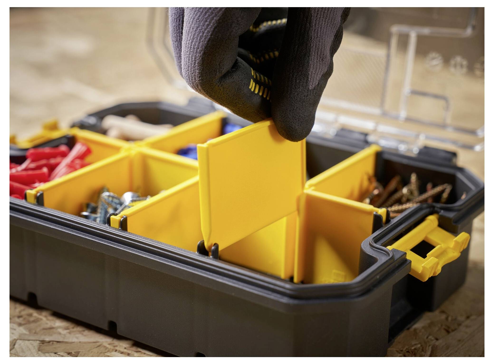 A gloved hand adjusts the compartment divider in a toolbox containing various screws and anchors, highlighting organization and storage.