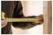 Person measuring wooden plank with a yellow tape measure.
