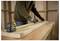 A person uses a tape measure to mark a piece of timber on a workbench in a workshop setting, focusing on precision and measurement.