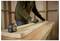 A person measures a wooden plank with a tape measure on a workbench, indicating carpentry or construction activity.