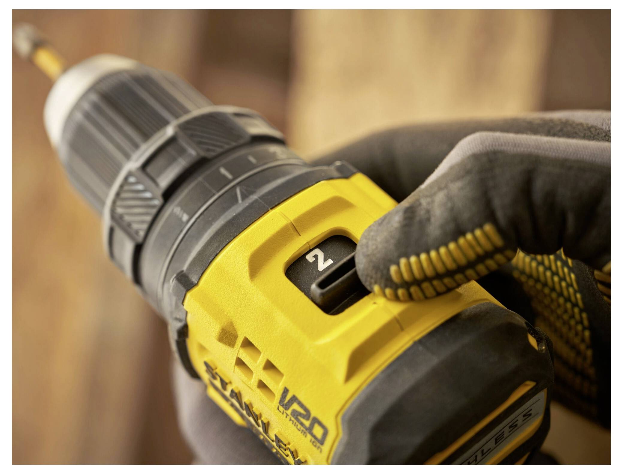 A close-up of a person's hand adjusting the speed setting on a yellow power drill with a gloved hand, focusing on the number '2'.