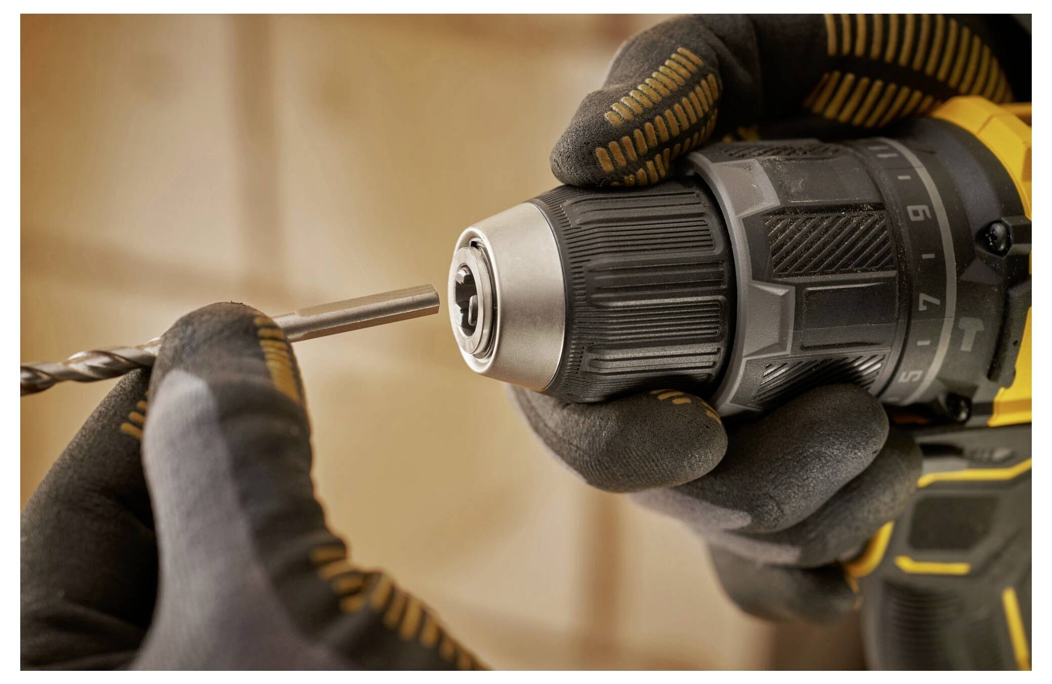 'Hands in gloves holding a drill, inserting a drill bit into the chuck, close-up view; focus on tool setup'