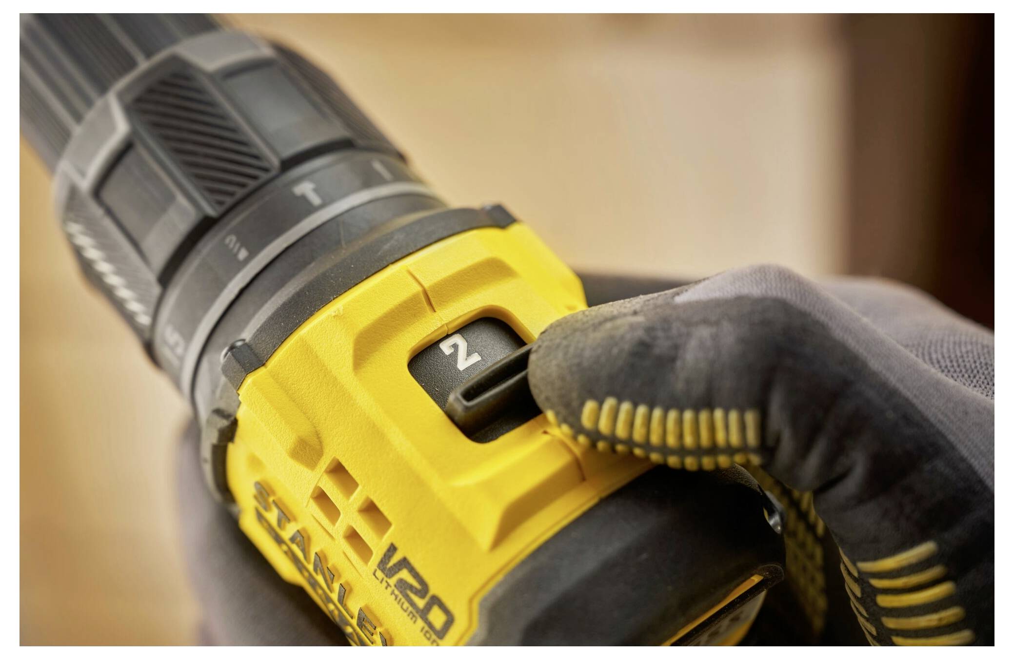 A gloved hand adjusts the torque setting on a yellow cordless drill, showing the number '2'.