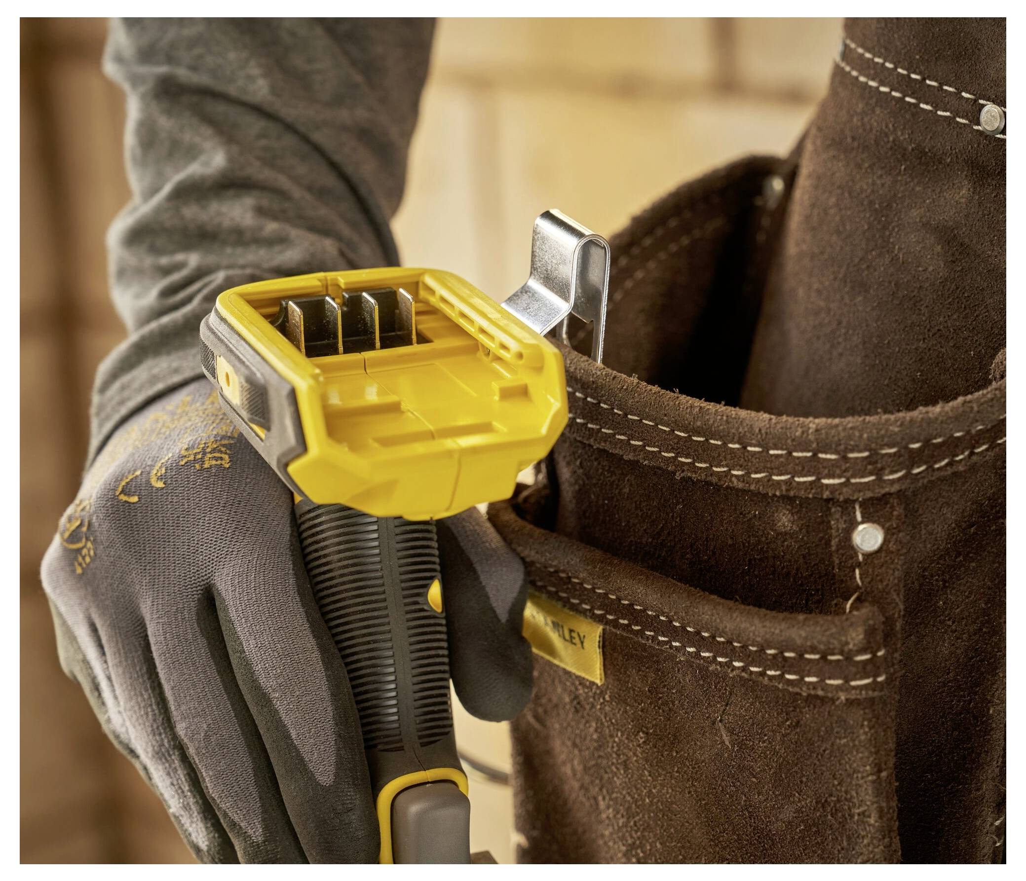 A person wearing gloves places a yellow utility knife back into a brown tool belt pouch, suggesting preparedness or work in progress.