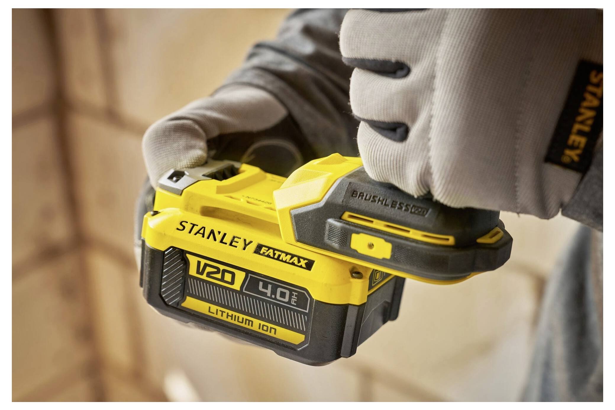 A person wearing gloves holds a Stanley Fatmax V20 4.0Ah lithium-ion battery, with a focus on the device's branding and design.