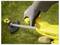 A person wearing gloves holds the handle of a yellow grass trimmer on a grassy area.