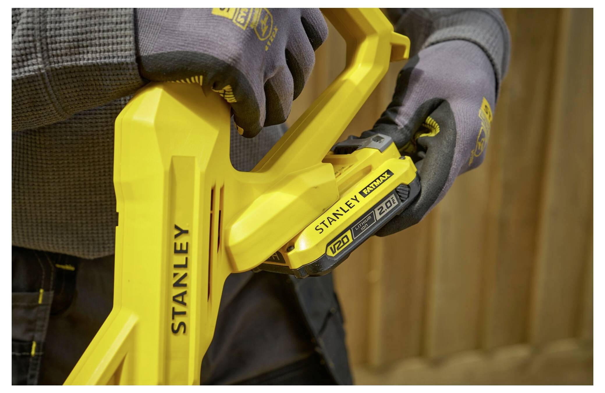 A person wearing gloves operates a yellow Stanley 20V Max lithium drill, adjusting the battery in a workshop setting.