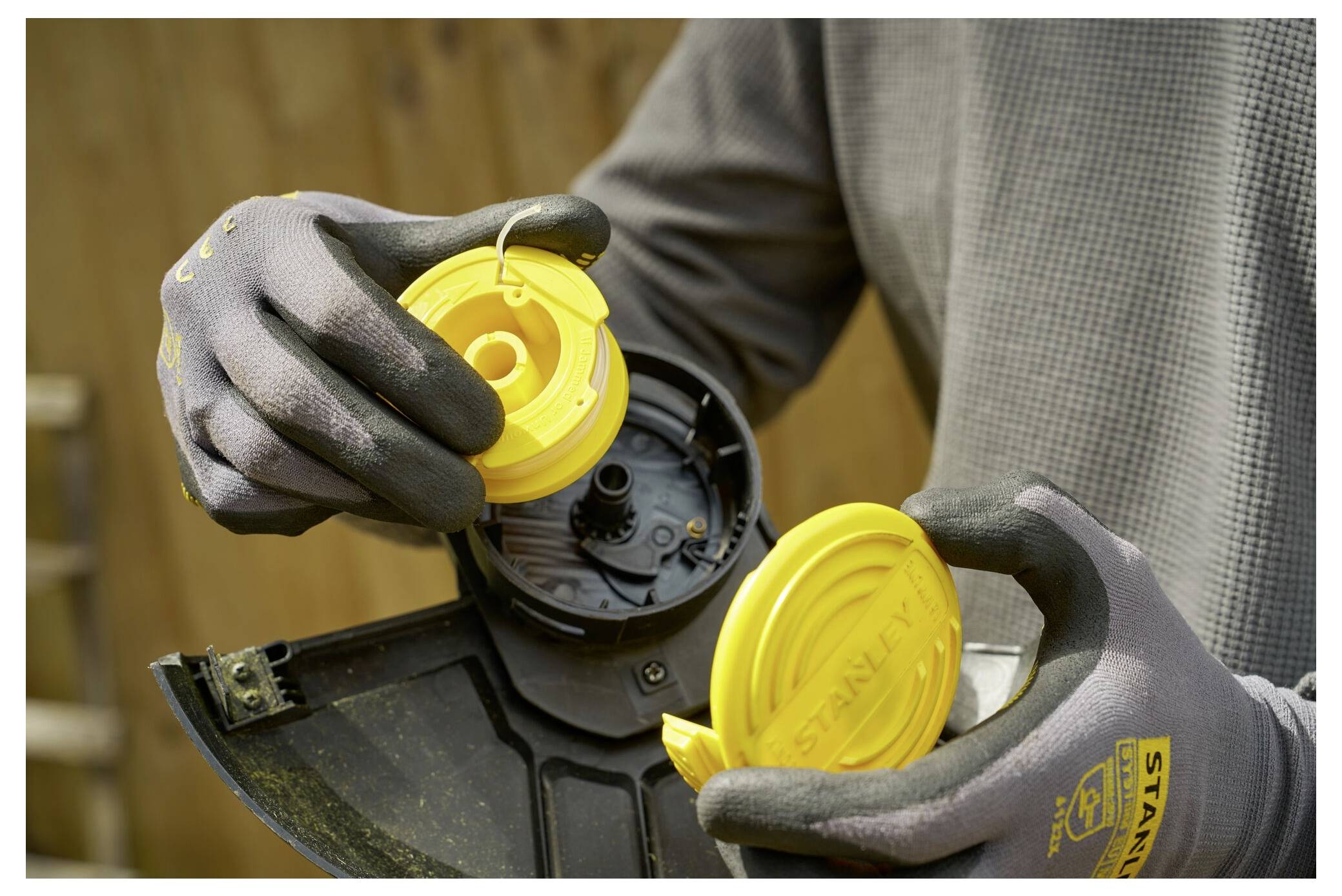 A person is wearing gloves while assembling or disassembling a yellow component of a garden tool or equipment, possibly a trimmer spool.