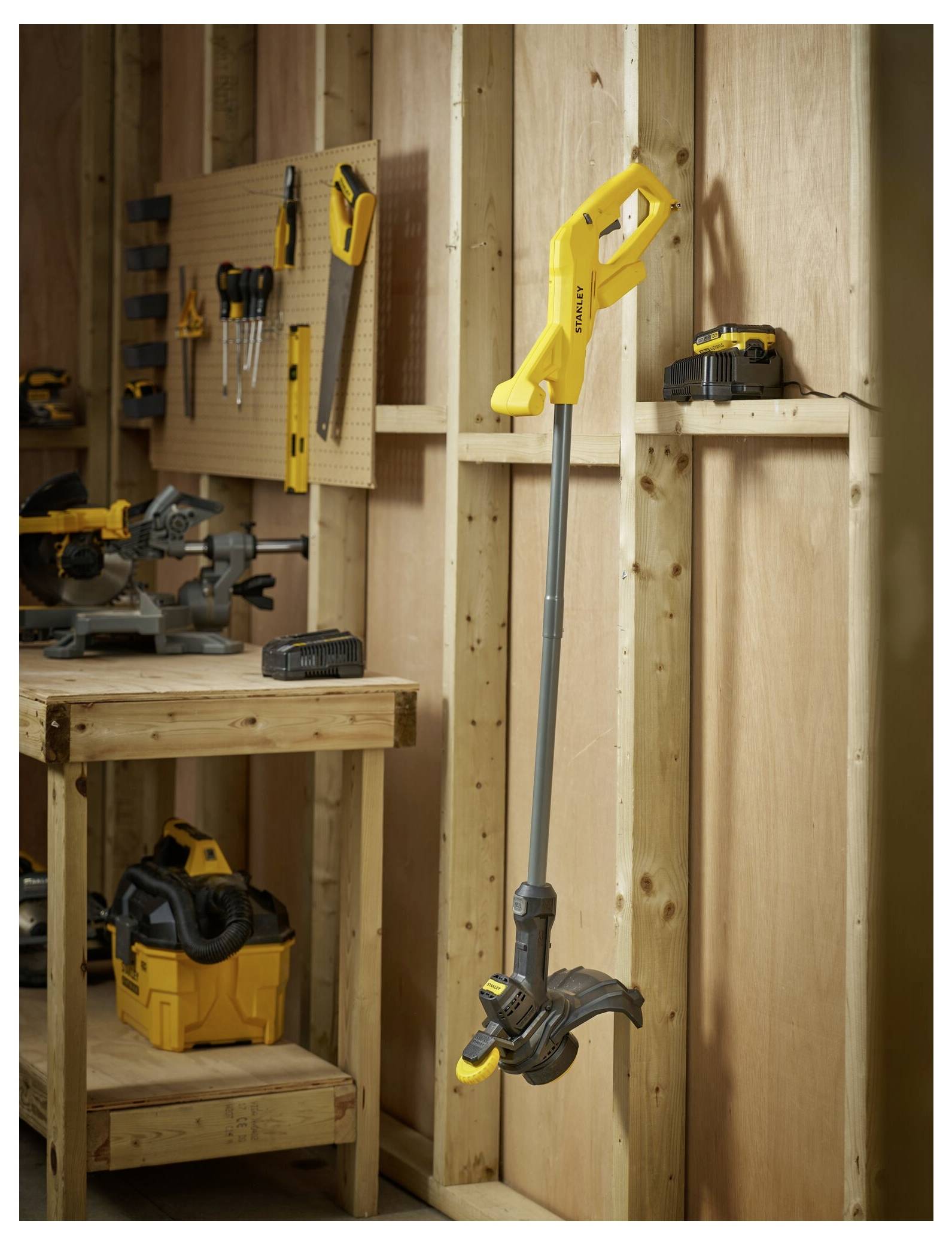 'A yellow garden tiller is hanging on a wooden wall in a workshop, surrounded by various tools and equipment on the bench and shelves.'
