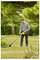 A person trims the grass using a yellow string trimmer in a garden surrounded by trees and shrubs.