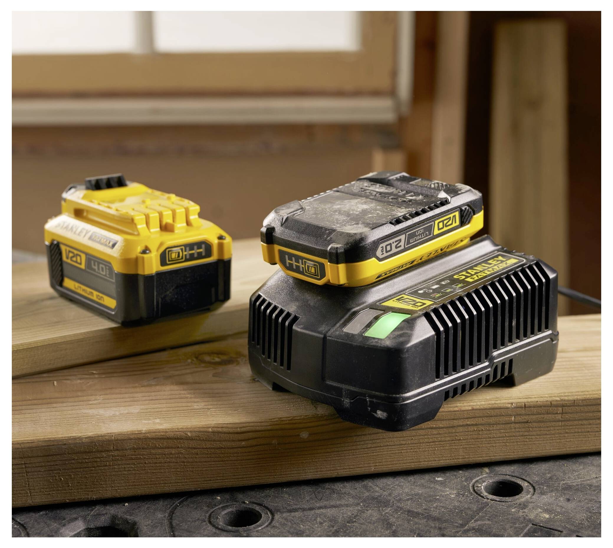 Two rechargeable power tool batteries on wooden planks in a workshop. One battery is prominently in the foreground, the other in the background.