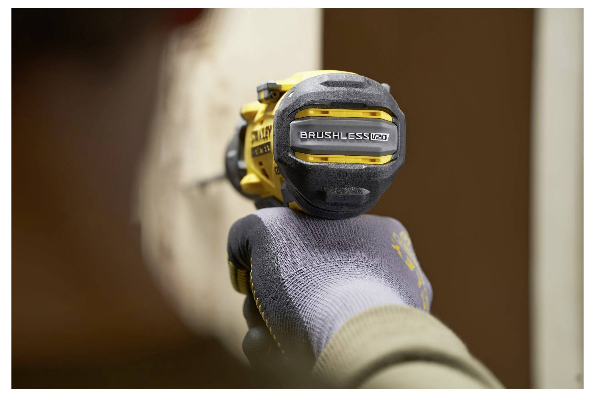 A person uses a yellow and black brushless drill against a surface, wearing a gray glove. The drill displays 'BRUSHLESS' text.