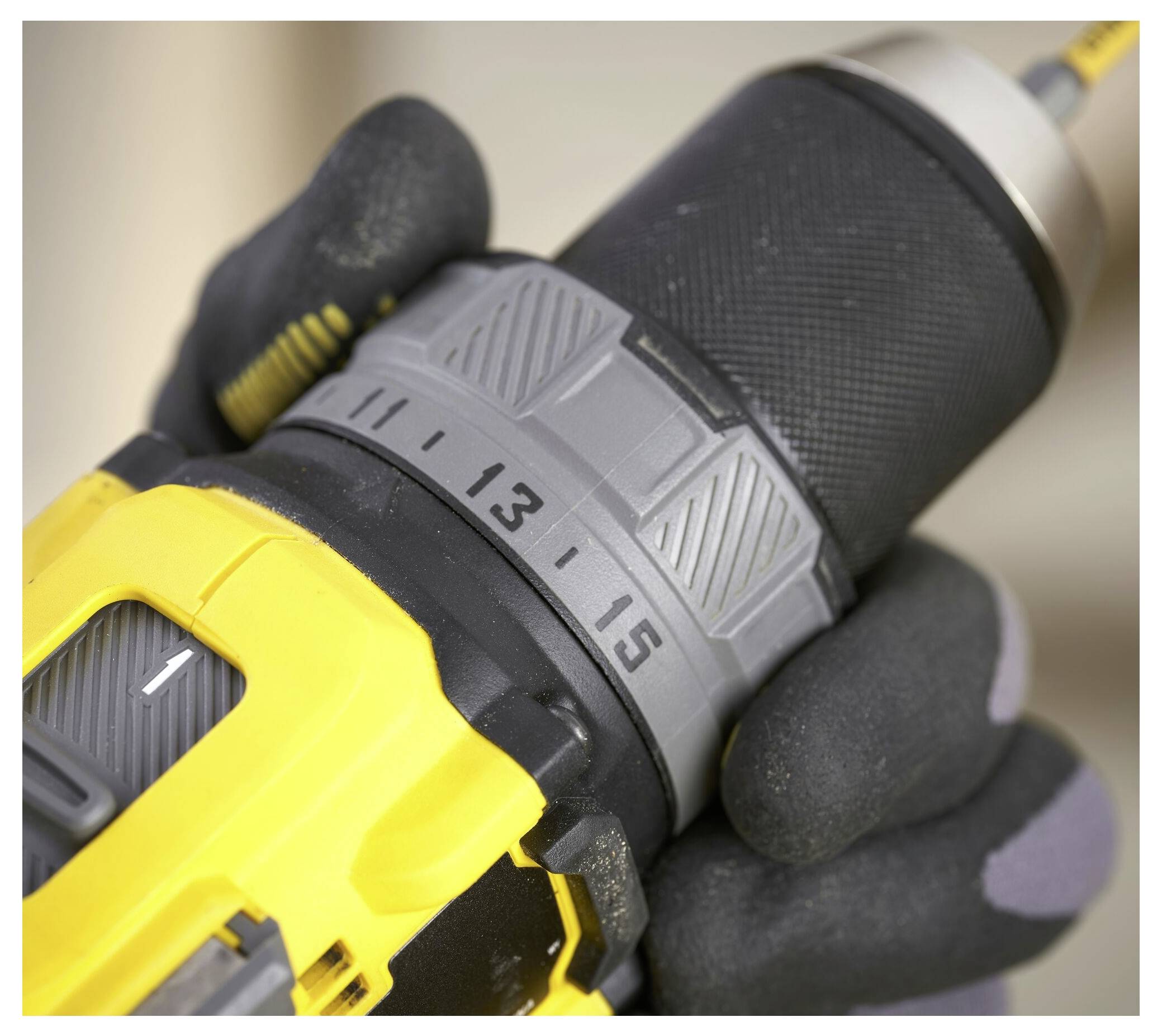 'Close-up of a person adjusting a yellow and black power drill with a gloved hand, focusing on the torque setting dial showing numbers 13 to 15.'